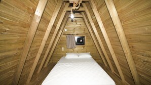 Une petite chambre mansardée en bois, avec un lit simple, une fenêtre avec un rideau et un plafond en pente.