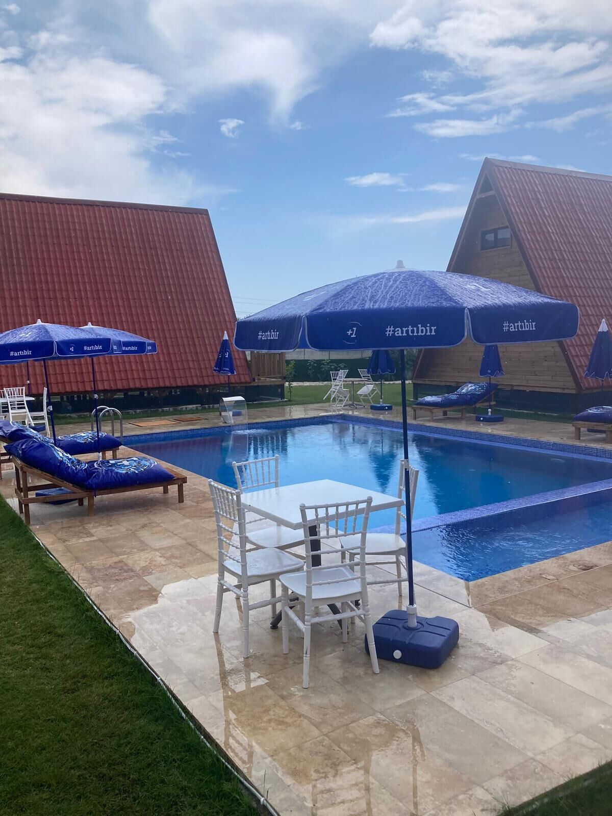 A swimming pool area with lounge chairs, umbrellas, and a table with chairs.