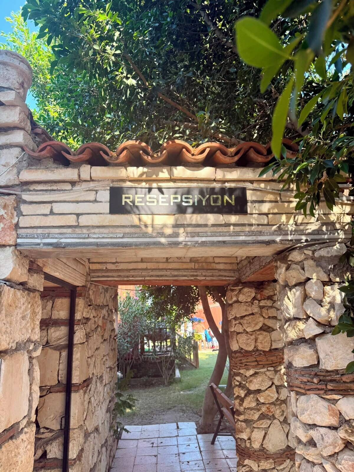 Un arco de piedra con un letrero que dice 'RESEPSIYON' que da acceso a una zona exterior cubierta.