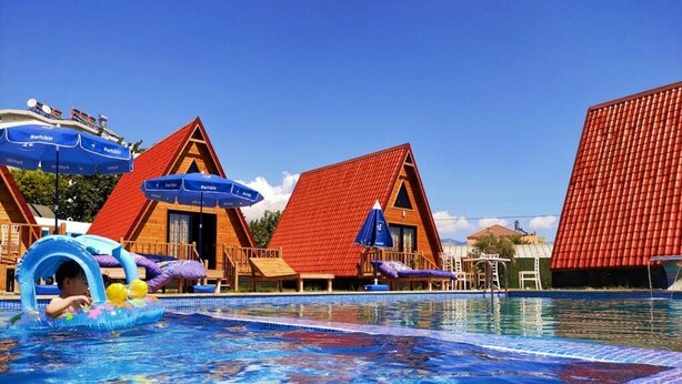 Une piscine entourée de bâtiments aux toits rouges, avec des chaises longues en bois et des parasols.
