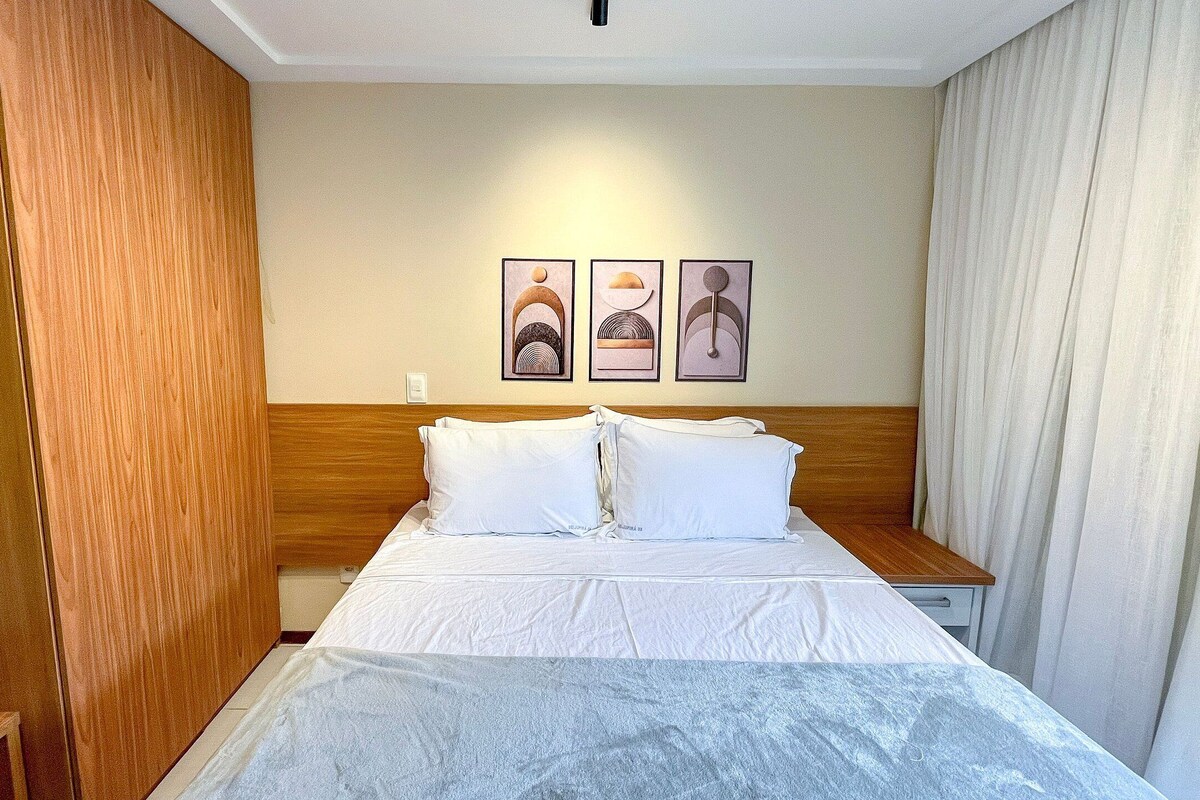 A hotel room with a bed, wooden headboard, white bedding, and three framed artworks on the wall.