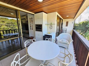 A balcony with a table and chairs, a kitchen area with an oven, and a view of greenery. - Nannai Residence (Ipojuca)