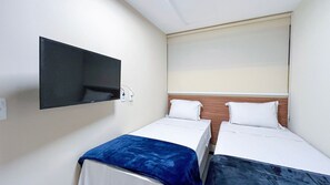A hotel room with two single beds, a TV mounted on the wall, and a window with a blind. - Nannai Residence (Ipojuca)