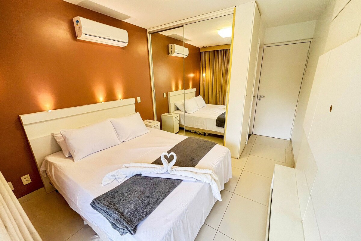 Quarto de hotel com cama, mesa de cabeceira, espelho, ar condicionado e guarda-roupa.