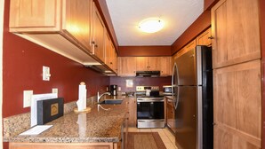A kitchen with wooden cabinets, granite countertops, stainless steel appliances, and a red wall.