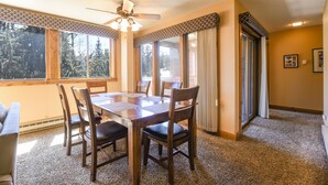 A dining area with a wooden table and chairs, large windows with curtains, and a ceiling fan.