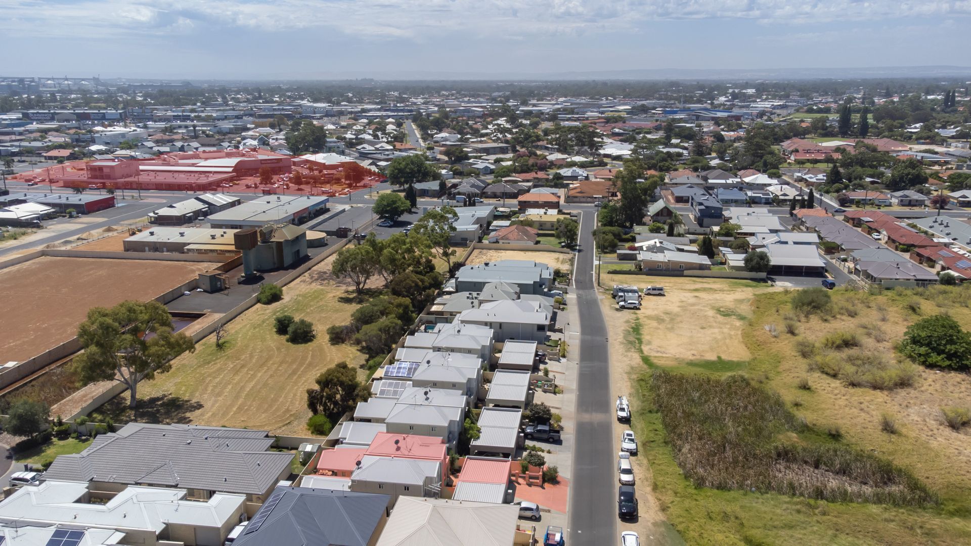 Vista aérea de una zona residencial con casas, una avenida principal y un gran edificio industrial al fondo.