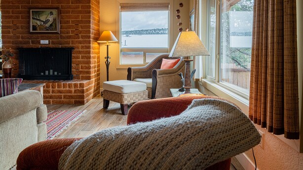 Un salon chaleureux avec une cheminée, un canapé confortable, un fauteuil et une grande fenêtre donnant sur l’extérieur.