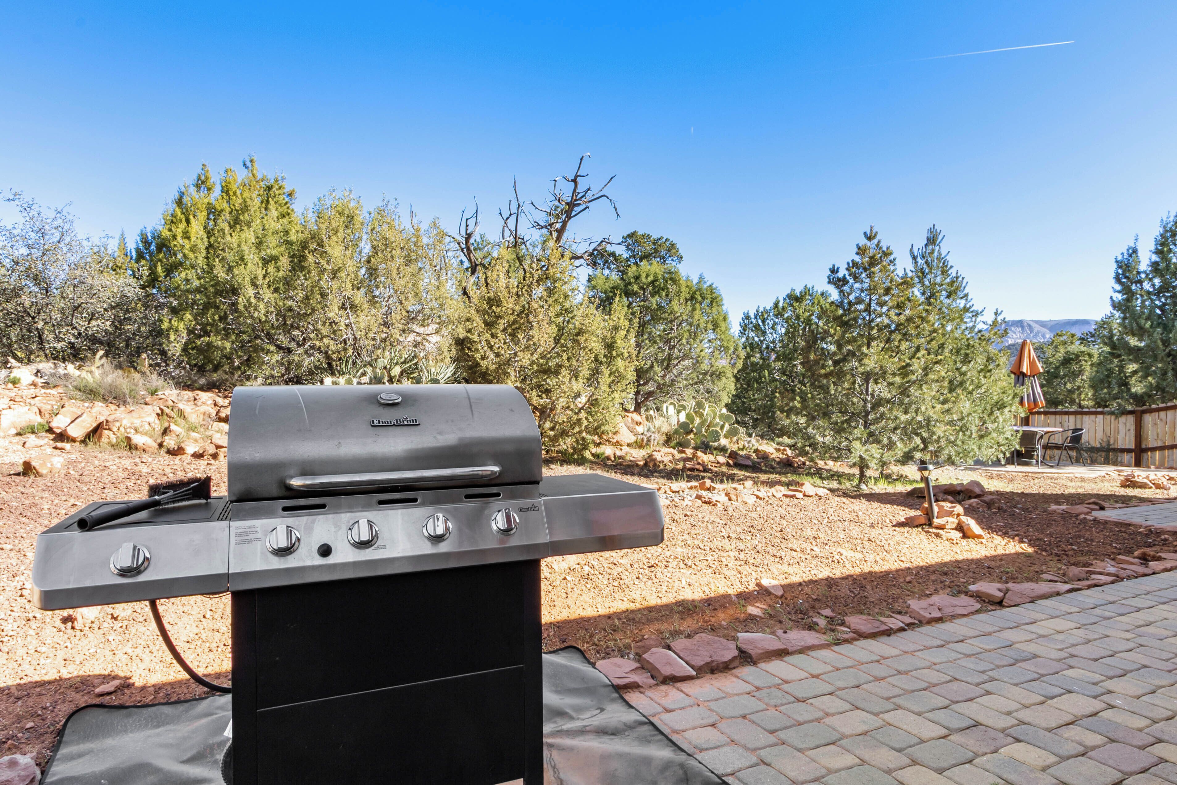 A barbecue grill in an outdoor setting with a clear sky and trees in the background.