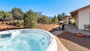 Un jacuzzi installé dans un jardin, avec une terrasse, un barbecue et une vue sur les montagnes.