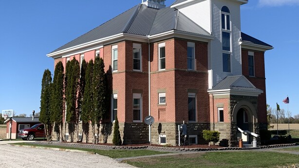 A large brick building with a central tower, likely a school, surrounded by well-maintained landscaping and a clear sky. - One-of-a-kind! Former Schoolhouse turned mansion for rent! The entire place!! (Port Austin)