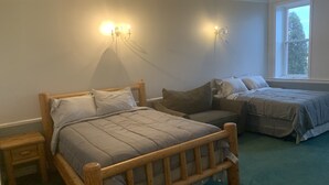 A bedroom with a large bed, two smaller beds, a nightstand, and a window. - One-of-a-kind! Former Schoolhouse turned mansion for rent! The entire place!! (Port Austin)