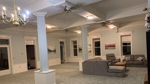 A spacious living room with a high ceiling, decorative columns, a chandelier, and a ceiling fan. - One-of-a-kind! Former Schoolhouse turned mansion for rent! The entire place!! (Port Austin)