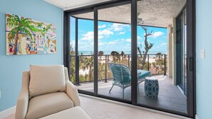 Un balcón con vista a la playa, una silla y un cuadro en la pared.