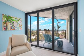 Ein Balkon mit Blick auf den Strand, ein Sessel und ein Bild an der Wand.