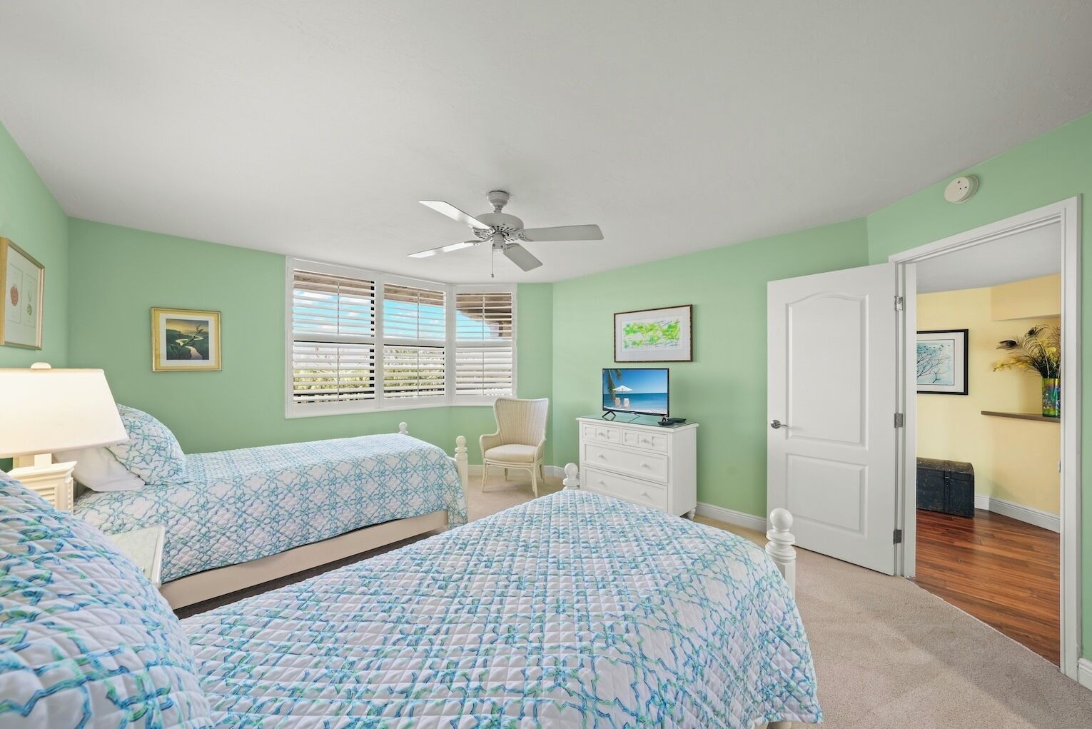A bedroom with two beds, a ceiling fan, a TV, and a door leading to another room.