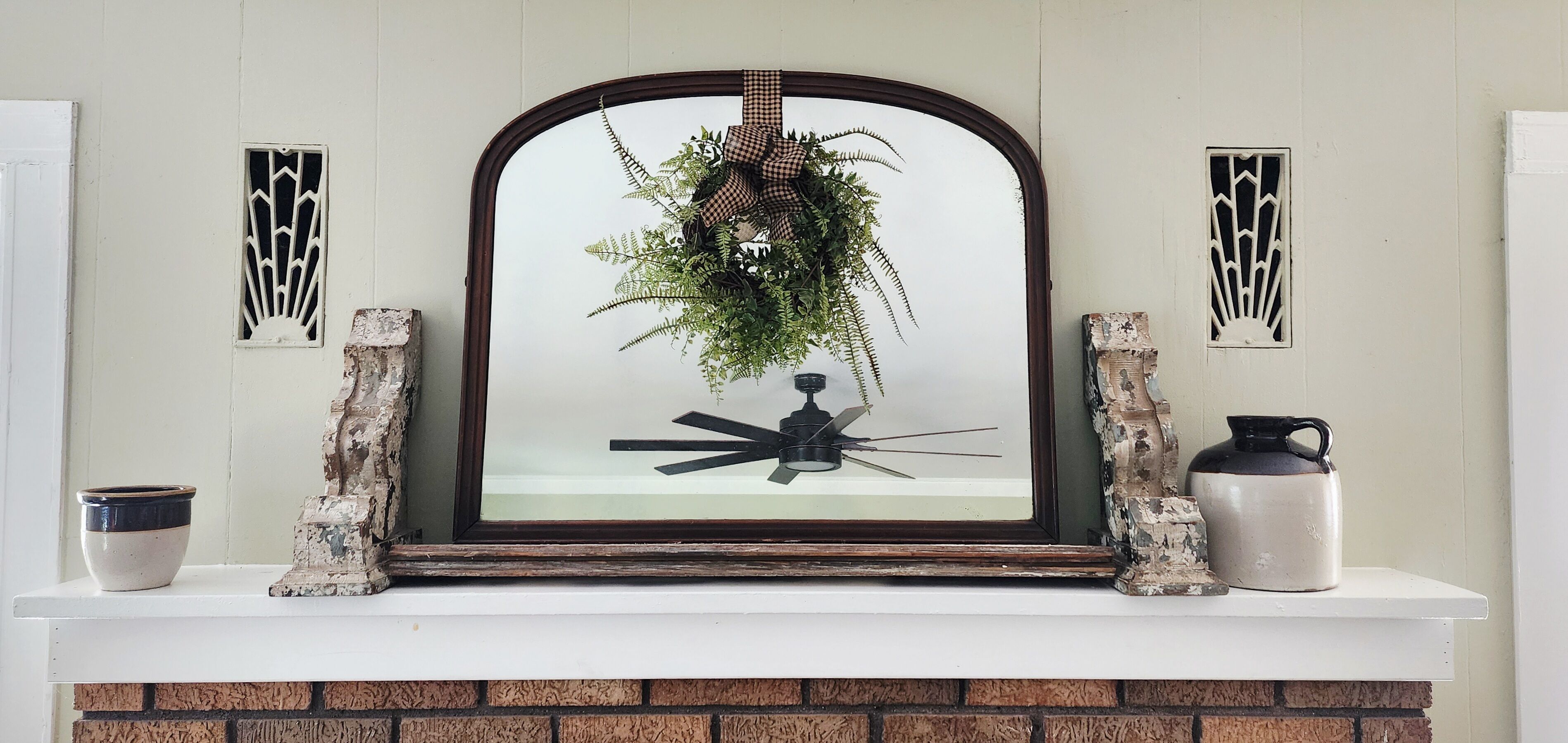 A fireplace with a decorative mirror, a hanging plant, and two wall-mounted sconces.