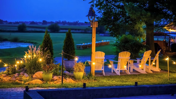 A deck with chairs and a bell, surrounded by potted plants and string lights. - The Cottage at Locavore Farm 32-Acre Prairie, Pond & Farm-to-Table Stay (Grant Park)