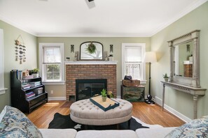 A living room with a fireplace, a round ottoman, a bookshelf, and a mirror.