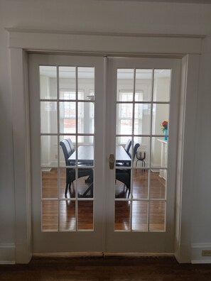 A white double door with glass panels, leading to a dining area with a table and chairs. - Peaceful House, Calming Gardens + Kitchen + Wi-Fi (Middleton)