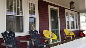 Eine Veranda mit zwei schwarzen und zwei gelben Adirondack-Stühlen, einer grünen Tür und einem weißen Geländer.