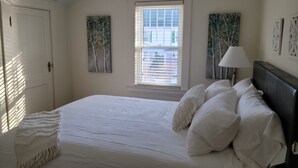 Ein Schlafzimmer mit einem großen Bett, einem Fenster mit Jalousien und zwei an der Wand hängenden Bildern.