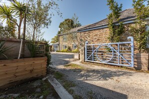 A stone building with a gated entrance, a gravel driveway, and a wooden planter with plants.