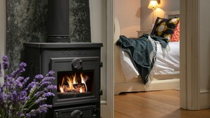 A room with a wood-burning stove, a bed with a white comforter and a blanket, and a lamp on the nightstand. - 5* Idyllic rural cottage, only 20 minutes from both North & South Cornish coasts (Truro)