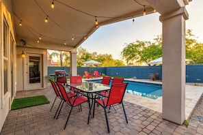 A covered patio with a pool, red chairs, and a barbecue grill.