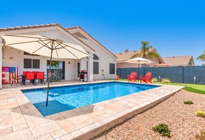 A swimming pool with a patio area, red chairs, and umbrellas.