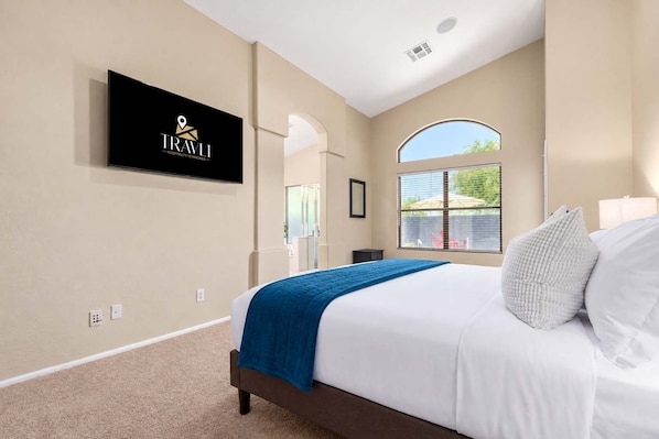 A hotel room with a bed, a TV mounted on the wall, a window with a view, and a door leading to another room.