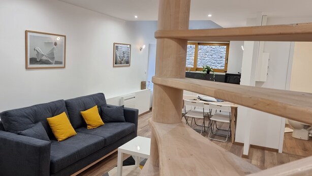 Un salon moderne avec un canapé gris et des coussins jaunes, une table basse blanche et un tapis à motifs géométriques.