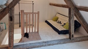Une chambre mansardée chaleureuse, avec une échelle en bois, un lit recouvert d’une literie à motifs et un petit tabouret en bois.