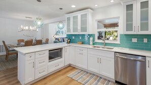 A modern kitchen with white cabinets, a stainless steel dishwasher, and a teal backsplash. - The Salted Coconut 3 Bedroom Home by RedAwning (Anna Maria)