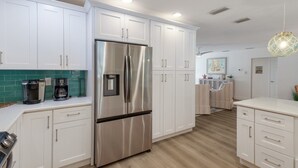 A modern kitchen with white cabinets, stainless steel appliances, and a wooden floor. - The Salted Coconut 3 Bedroom Home by RedAwning (Anna Maria)
