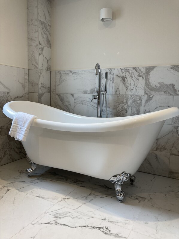 Una bañera independiente en un baño con paredes y piso de mármol.
