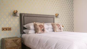 A neatly made bed with a grey headboard, two bedside lamps, and patterned wallpaper.