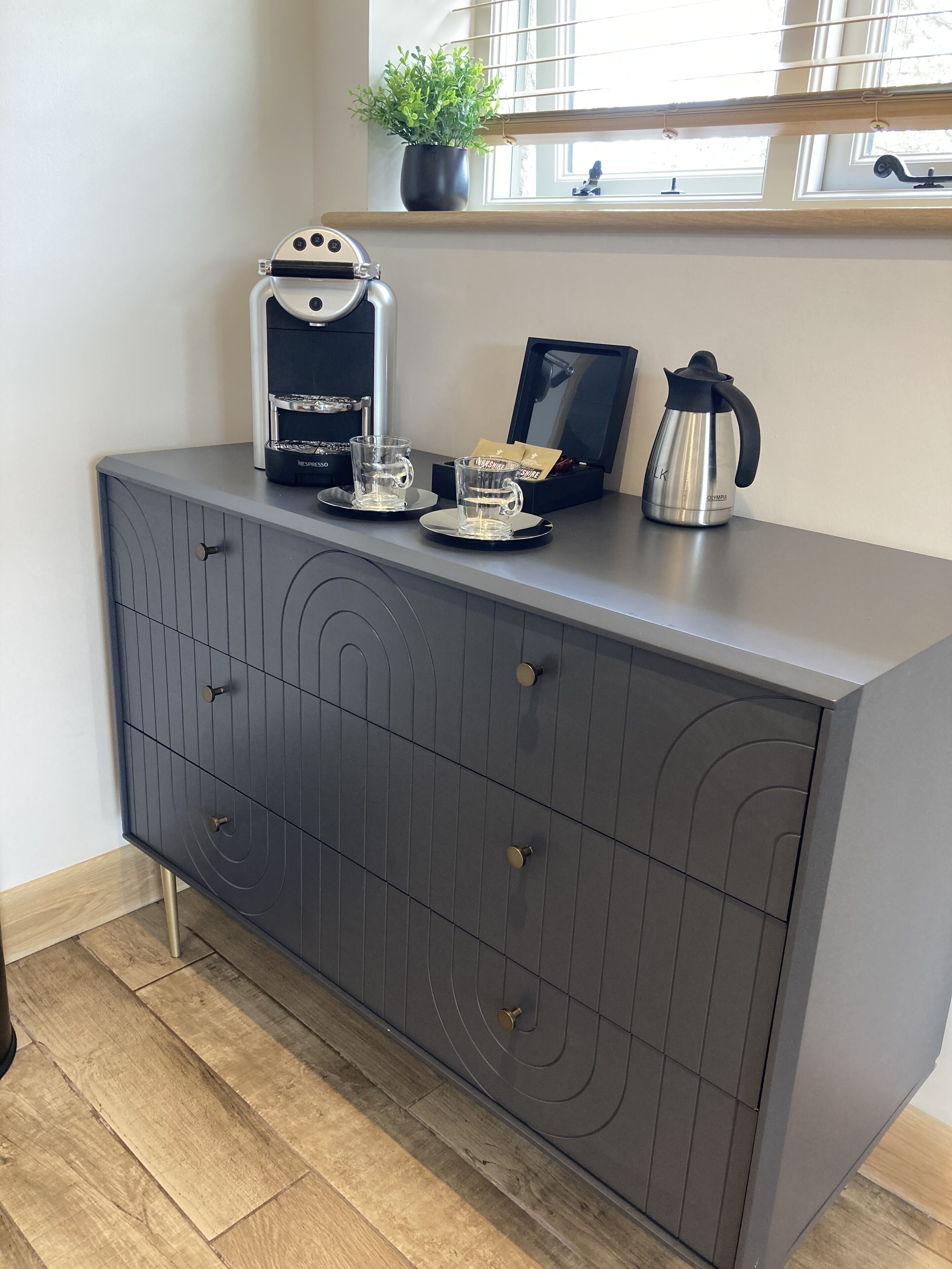 A modern kitchen with a built-in espresso machine, a coffee maker, and two glass cups on a dark grey cabinet.
