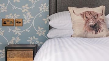 A bedroom with a bed, a nightstand, a wall-mounted lamp, and a floral wallpaper pattern.