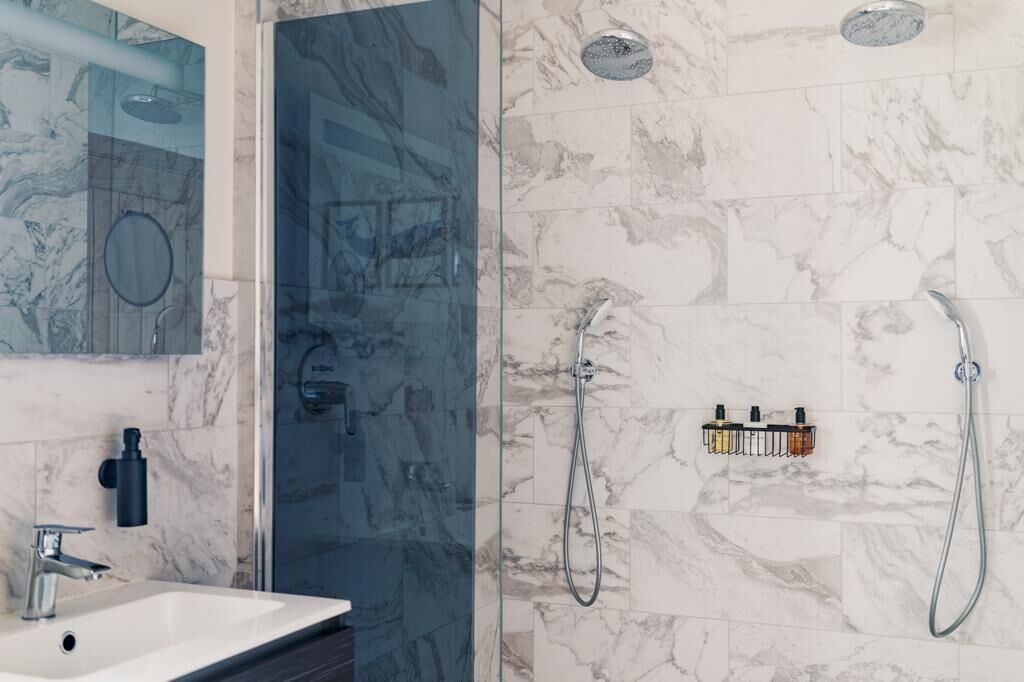 A modern bathroom with a glass shower enclosure, a marble-tiled shower area, a sink with a faucet, and a mirror.