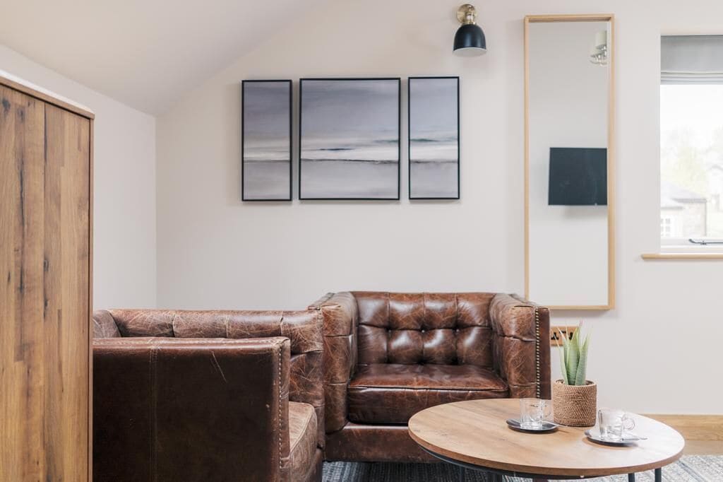 Ein Wohnzimmer mit einem braunen Ledersofa, einem runden Couchtisch und drei gerahmten Kunstwerken an der Wand.