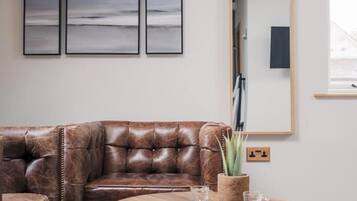 A living room with a brown leather sofa, a round wooden coffee table, and three framed artworks on the wall.