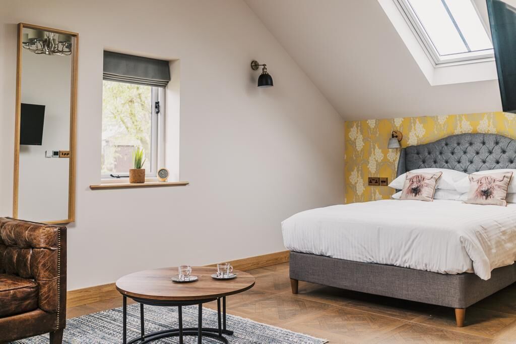 A bedroom with a bed, a chair, a round table, a mirror, a window, and a ceiling light.