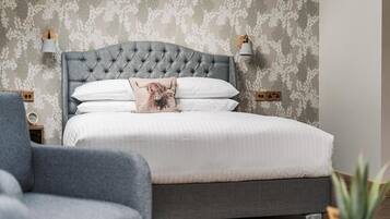 Un dormitorio con cabecera capitonada, ropa de cama blanca, una almohada decorativa y un sillón gris.