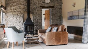 A cozy living room with a stone wall, a fireplace, a sofa, and a chair. - The Blind Bull (Buxton)