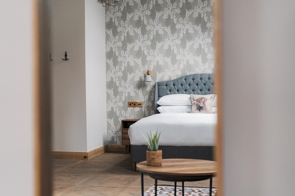 Une chambre à coucher avec une tête de lit capitonnée, une table de chevet, une lampe et une plante en pot.