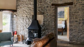 A cozy room with a stone wall, a black wood-burning stove, a bed, and a clock. - The Blind Bull (Buxton)