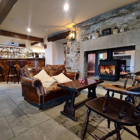 A cozy living room with a stone fireplace, leather sofa, wooden table, and bar area with stools.