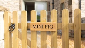 A wooden gate with a sign reading "MINI PIG" in front of a stone building. - The Blind Bull (Buxton)