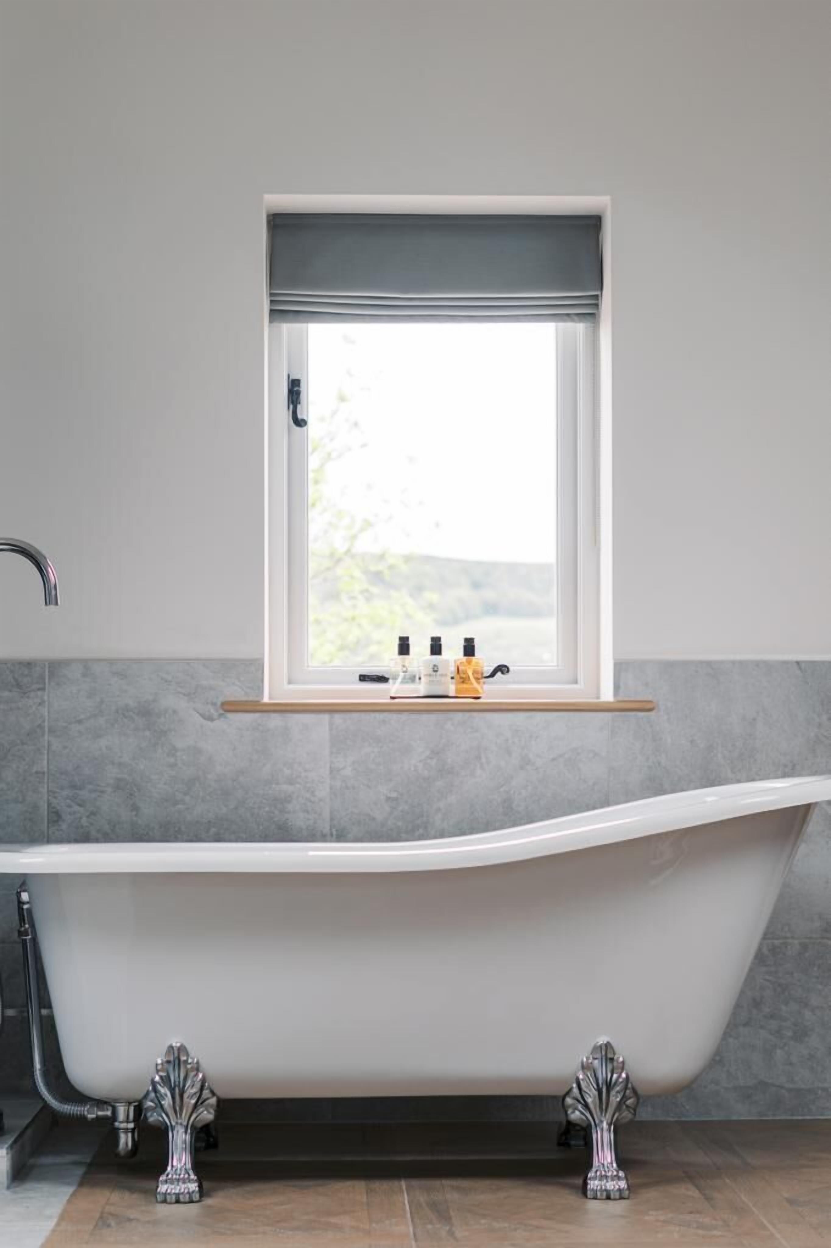 Une salle de bain moderne avec une baignoire sur pieds, une fenêtre offrant une belle vue et une étagère contenant des articles de toilette.